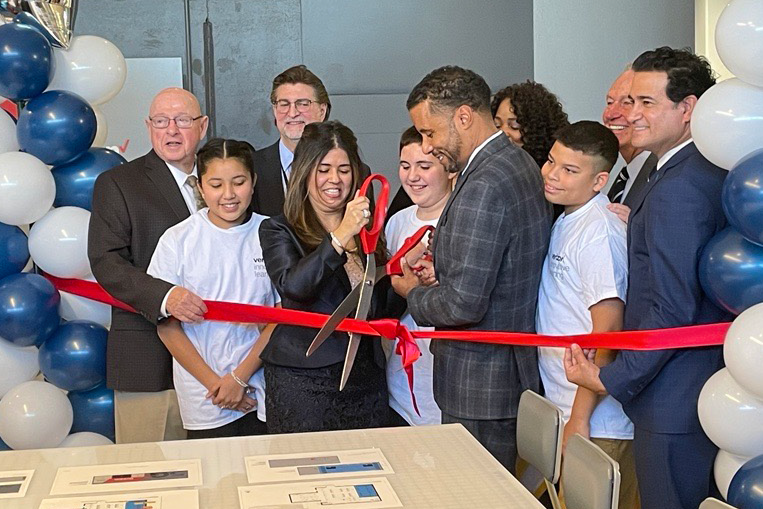 People gathered, a person cutting a ribbon, balloons around them and a table.