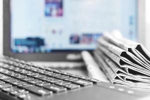 A pile of newspapers next to a keyboard and close to a computer screen